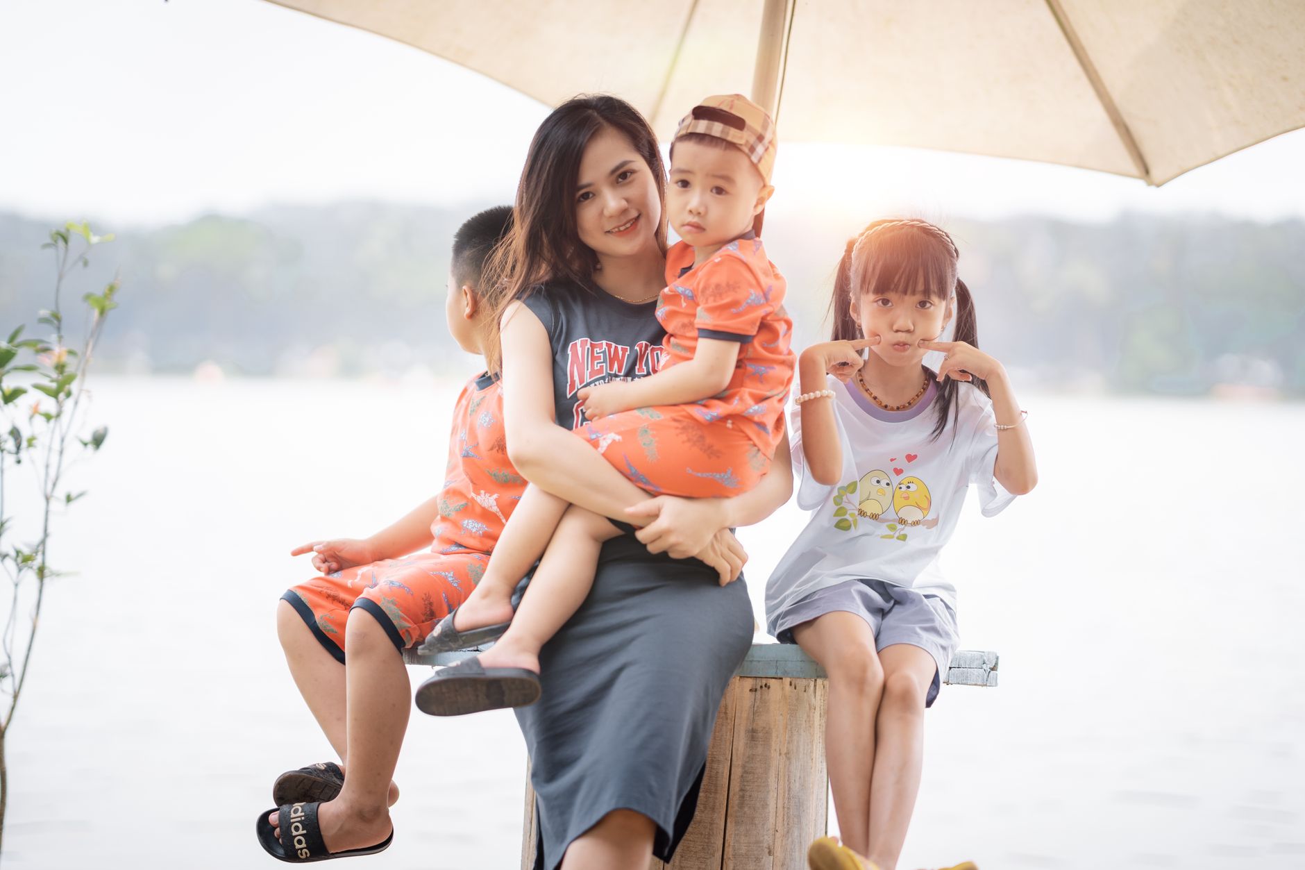 A mother and her children enjoying time by the lake under an umbrella during summer.