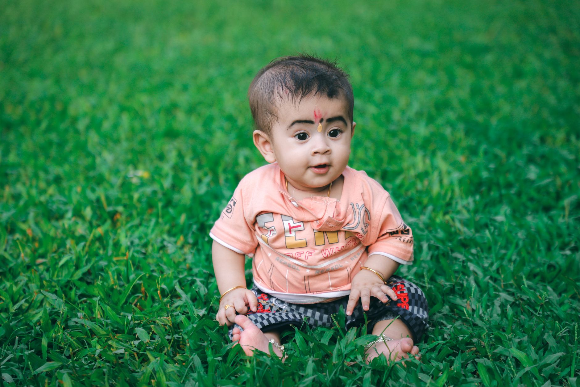 Charming portrait of a baby boy seated on vibrant green grass, exhibiting a joyful expression.